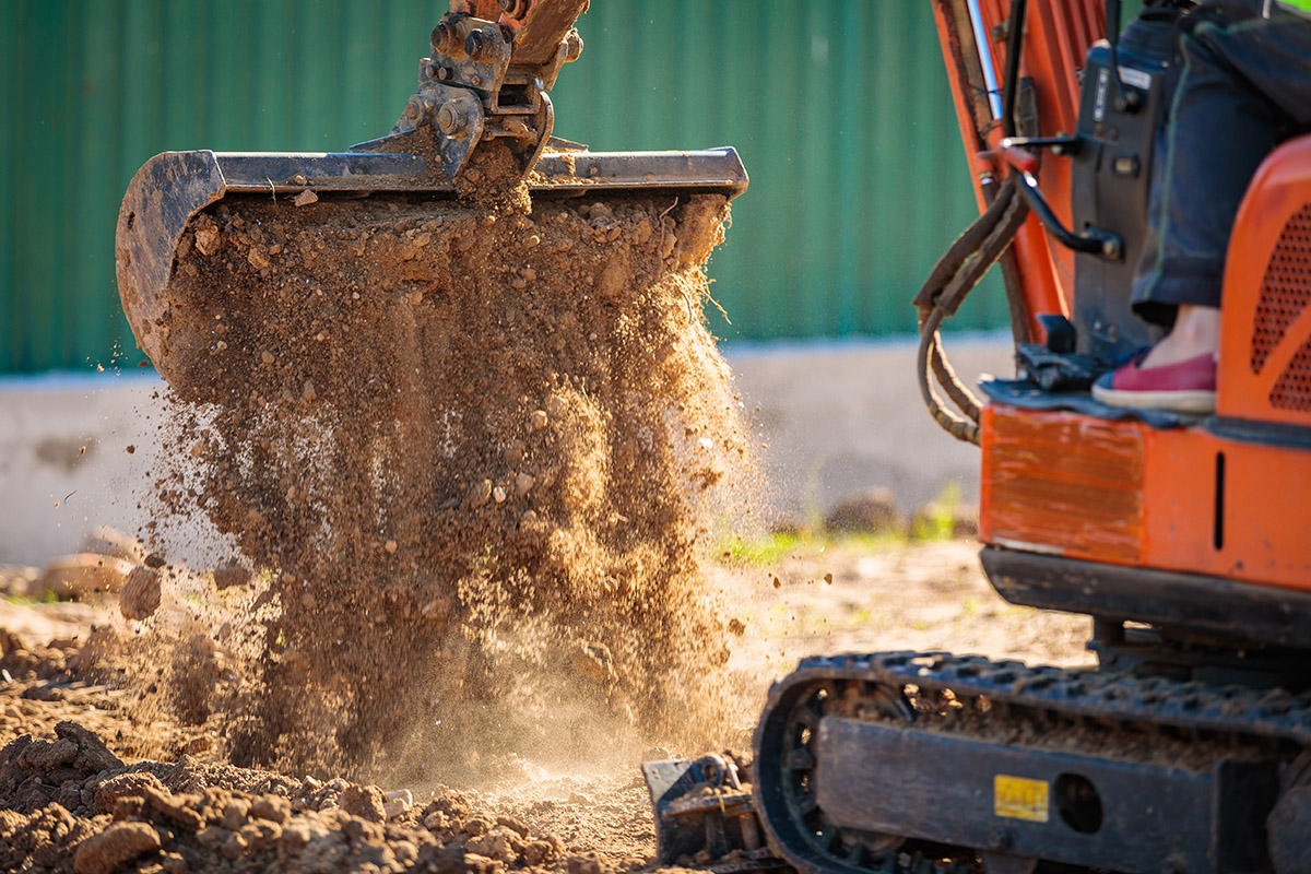 A mini excavator rakes the earth with a bucket.